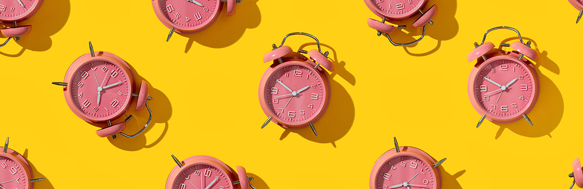 A photograph of multiple pink alarm clocks arranged in a pattern on a bright yellow background.