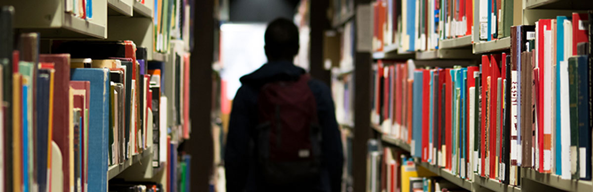 Student with backpack walking down library aisle